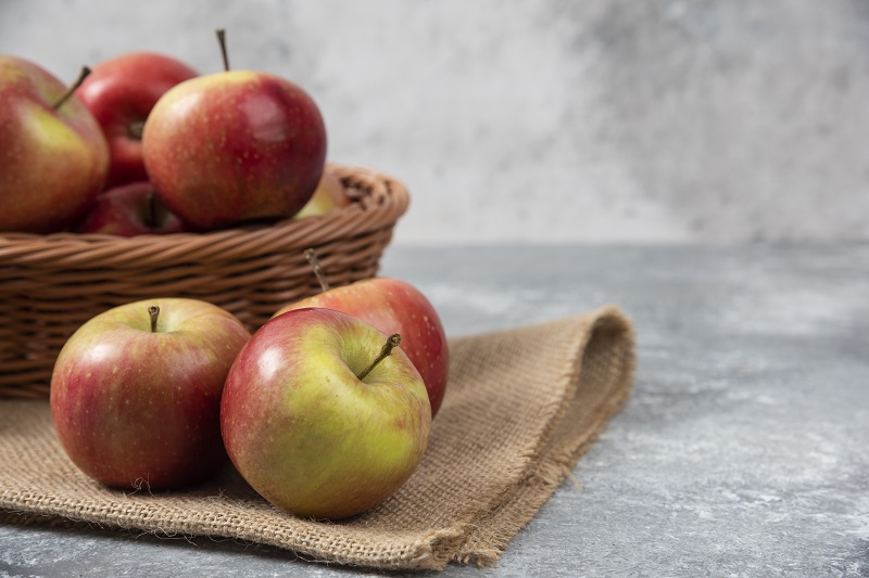Wicker basket of ripe shiny apples on marble surface