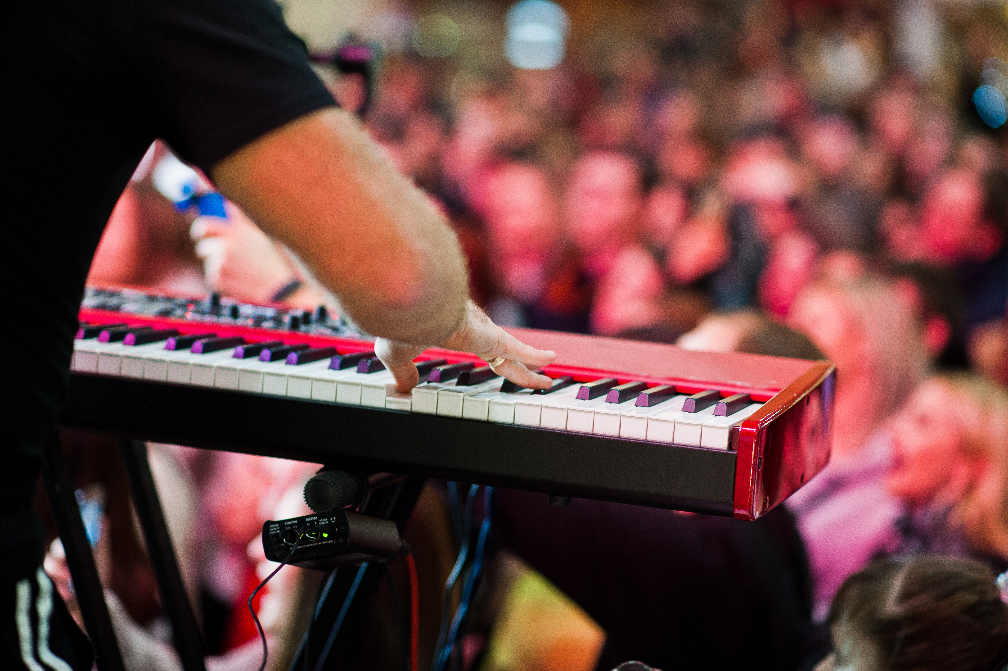 Artist play on audio piano on stage in a concert hall behing peoples.